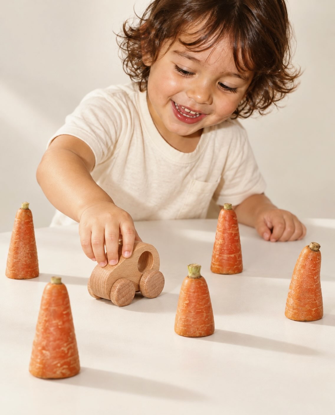 A smiling child pushing a wooden Blesii car between carrot roadblocks